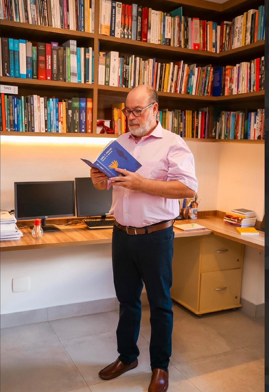 Fábio Sigaud Furquim lendo no consultório de psicologia em Águas Claras, Brasília, diante das estantes de livros